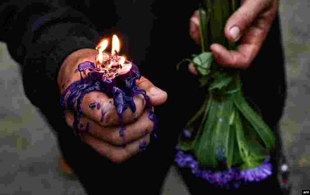 Un devoto sostiene una vela encendida en su mano y un ramo de flores moradas, en tributo a San Lázaro.