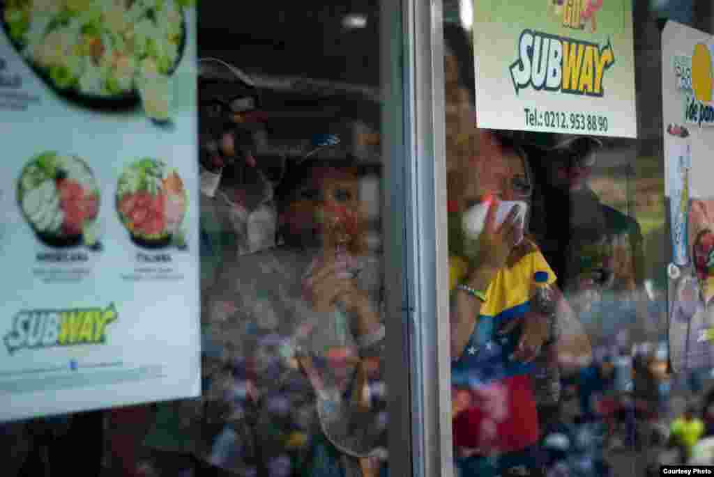 Manifestantes se resguardan en establecimiento de comida rápida Subway y observan el enfrentamiento entre manifestantes y efectivos de la PNB. (Foto: Juan Pablo Arraez)