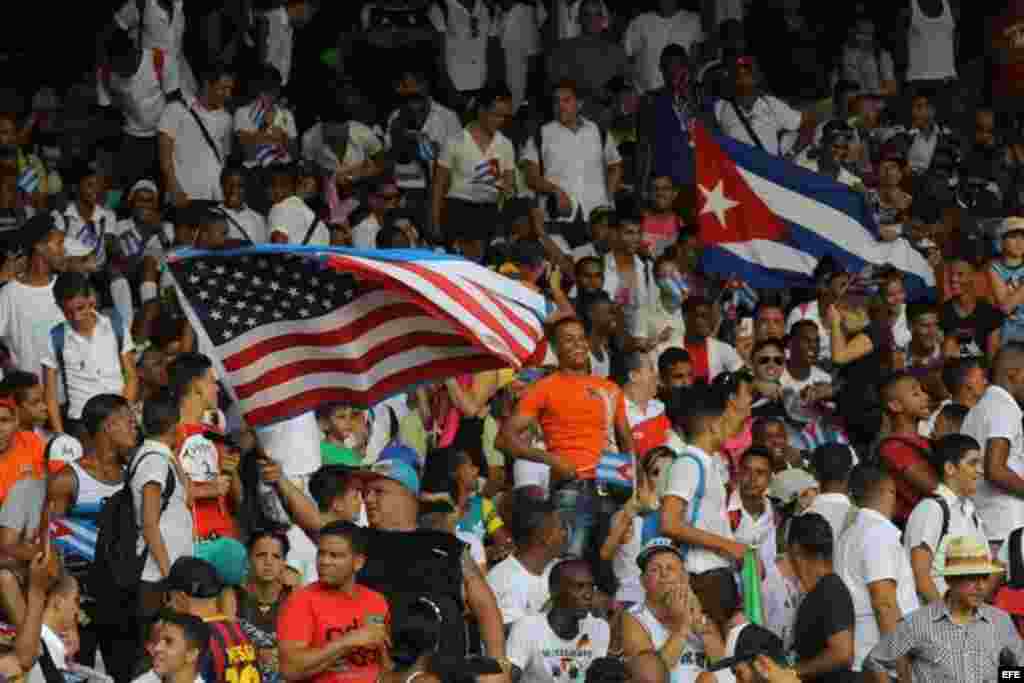 Un aficionado al fútbol porta una bandera cubana, mientras otro hace ondear la estadounidense, en el  partido amistoso entre Cuba y Estados Unidos, en el estadio Pedro Marrero en La Habana, donde los visitantes ganaron dos goles a cero.  
