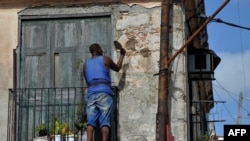Un hombre repara la fachada de un viejo edificio en La Habana.