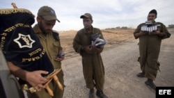 Soldado israelíes cargan con una Torá y libros de rezo mientras otros soldados se preparan para desplegarse junto a la frontera con Gaza, en Israel.