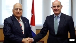 El ministro español de Economía y Competitividad en funciones, Luis de Guindos (d), y el vicepresidente del Consejo de Ministros de Cuba, Ricardo Cabrisas Ruiz (i), se saludan durante la firma de los acuerdos para reestructurar la deuda cubana con España
