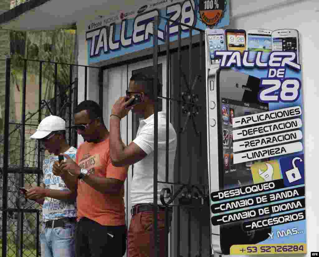 Varios jóvenes revisan sus móviles a las puertas de un negocio privado de reparaciones de teléfonos en La Habana.