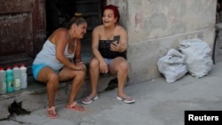 Dos mujeres cubanas conversan mientras chequean un mensaje en el celular.