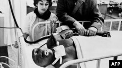 La esposa de Benny "Kid" Paret y su manager, Manuel Alfaro, junto al boxeador, inconsciente en una cama del hospital Roosevelt, tras la pelea con Emile Griffith, en marzo de 1963. (Foto AFP/Archivo)