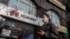 Mujer con mascarilla delando de una tienda de la empresa Huawei en China.